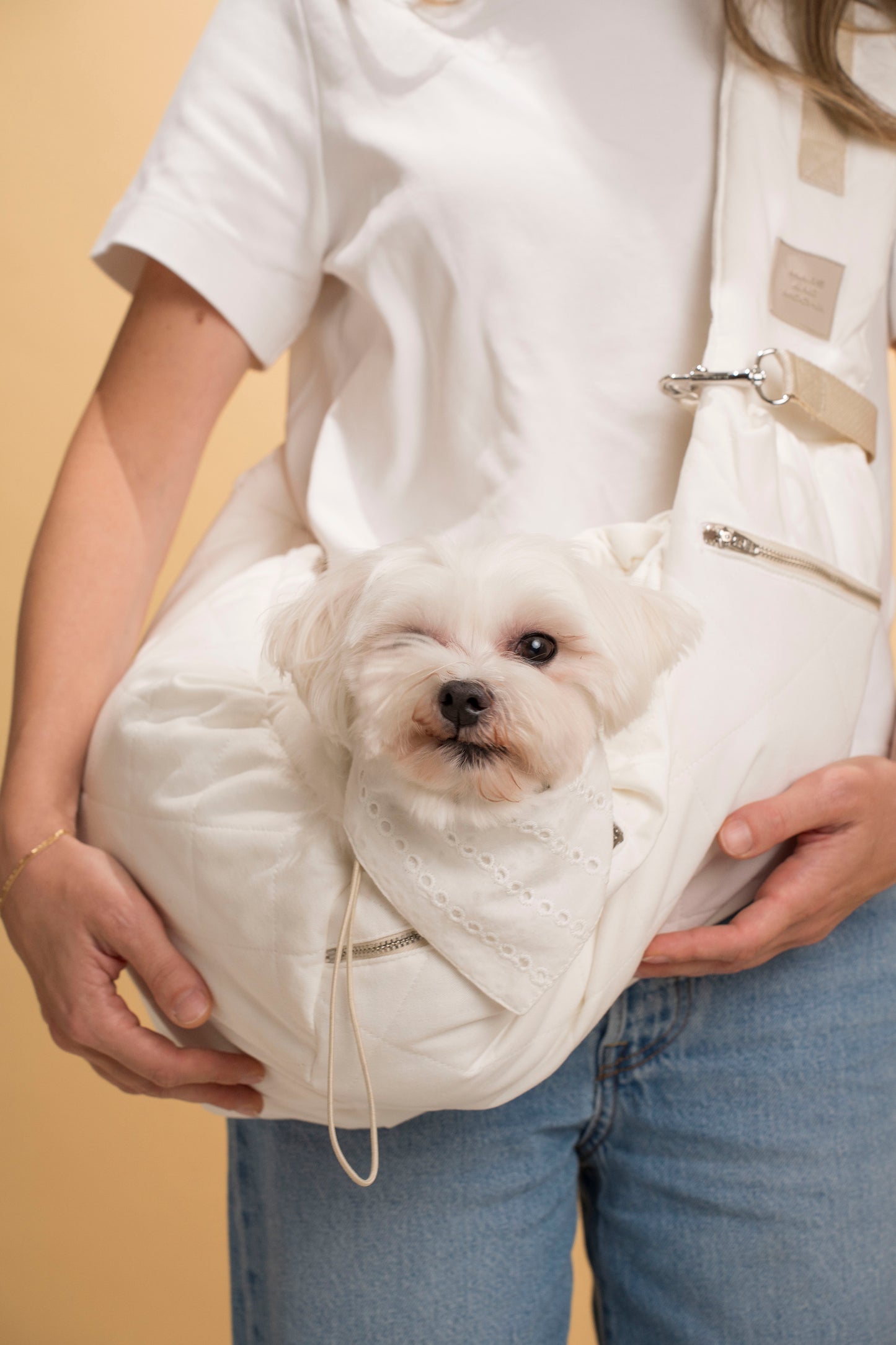 Beige dog sling carrier for hands-free walking and secure transport of small pets.